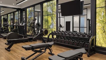 Un gimnasio con equipo de ejercicio, estantes para pesas y grandes ventanales con vistas a árboles.