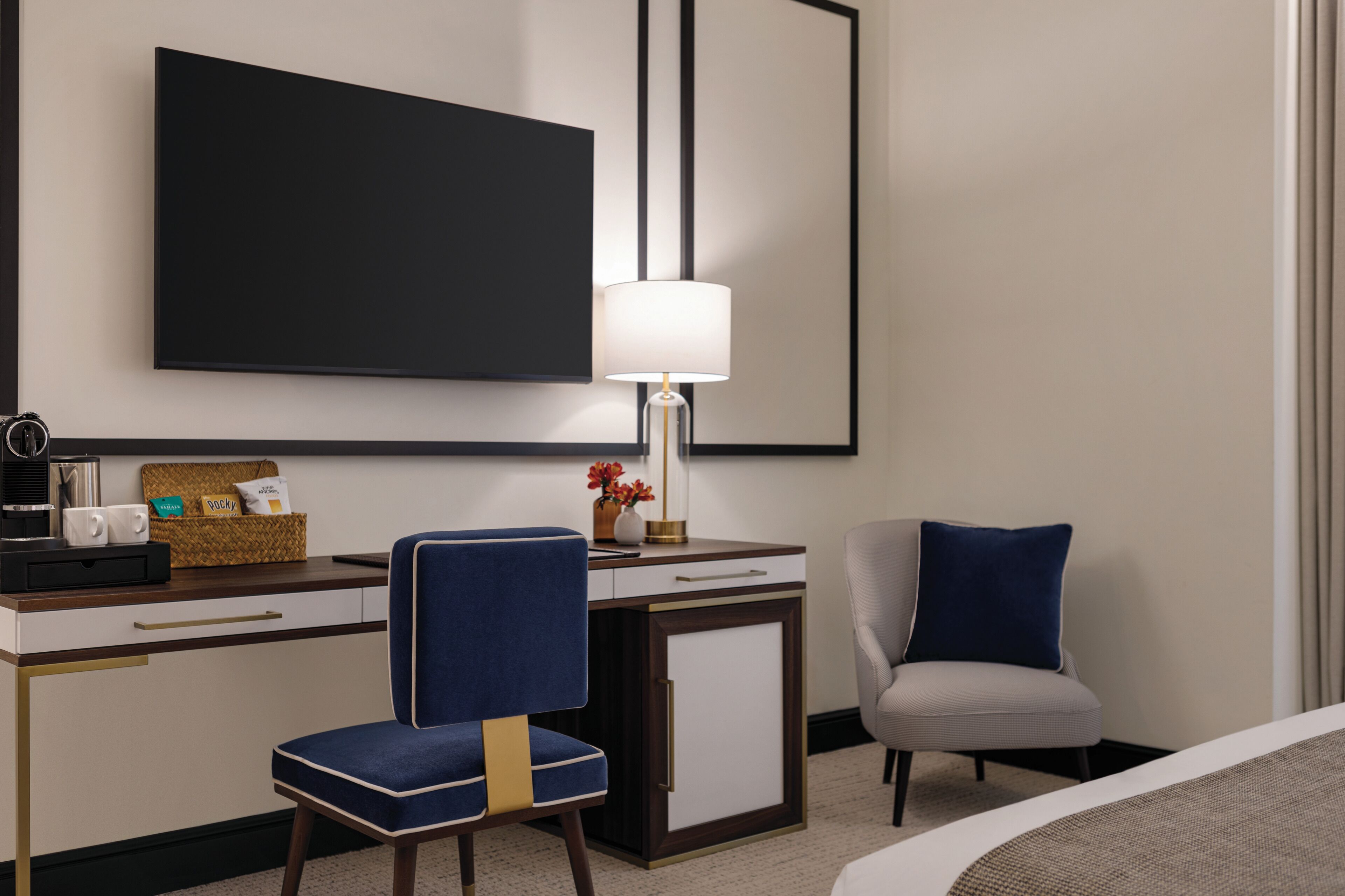 Une chambre d’hôtel équipée d’un bureau, de deux chaises, d’une lampe, d’une machine à café et d’un téléviseur à écran plat.