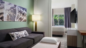 A hotel room with a sofa, a bed, a desk, a lamp, and a TV.