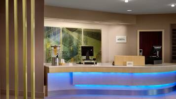 Un mostrador de recepción con una barra iluminada en azul, un letrero que dice "BONVOVY" y un muro de cristal con texto.
