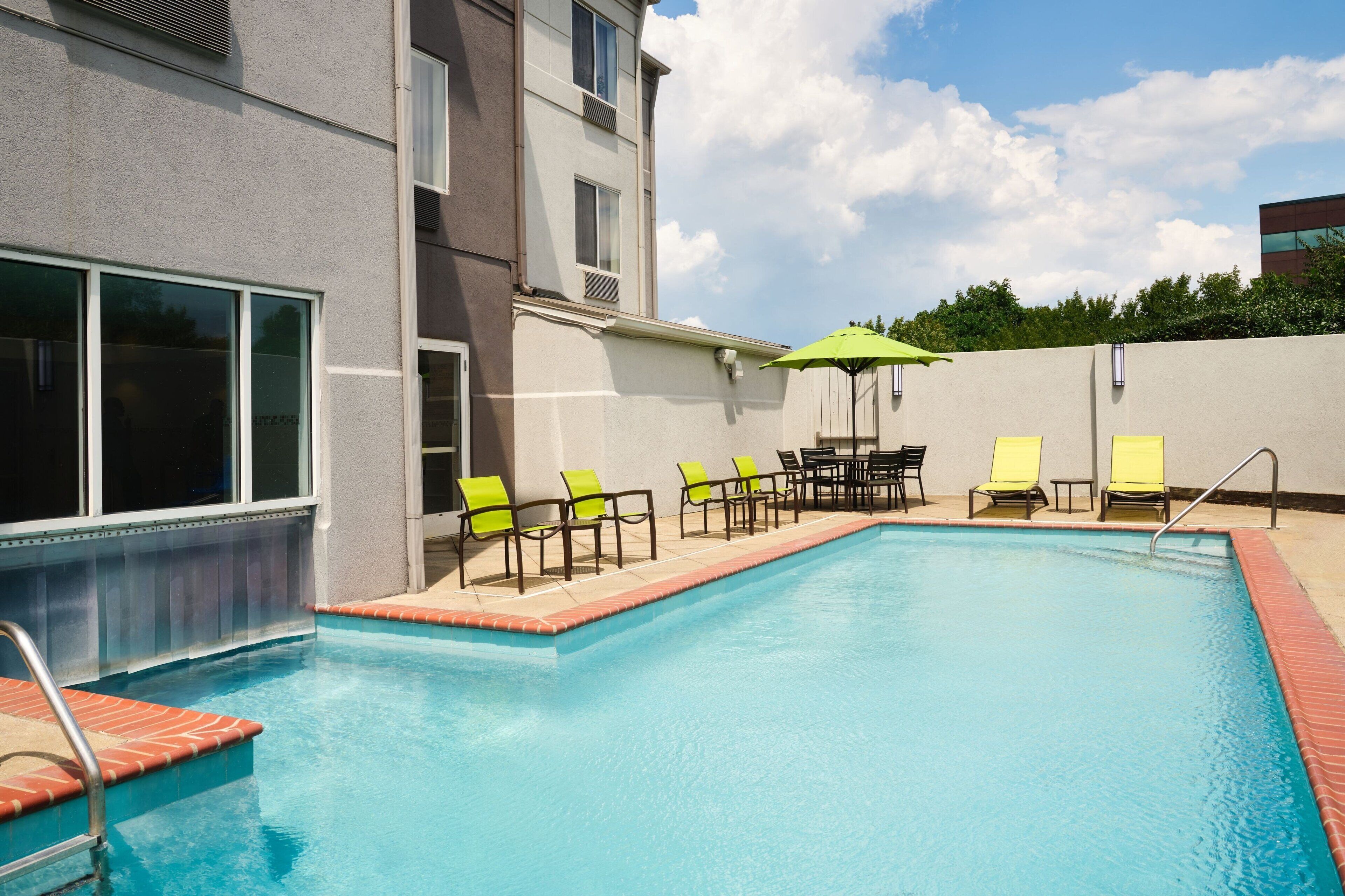 A swimming pool with chairs and a table, surrounded by a building with large windows.