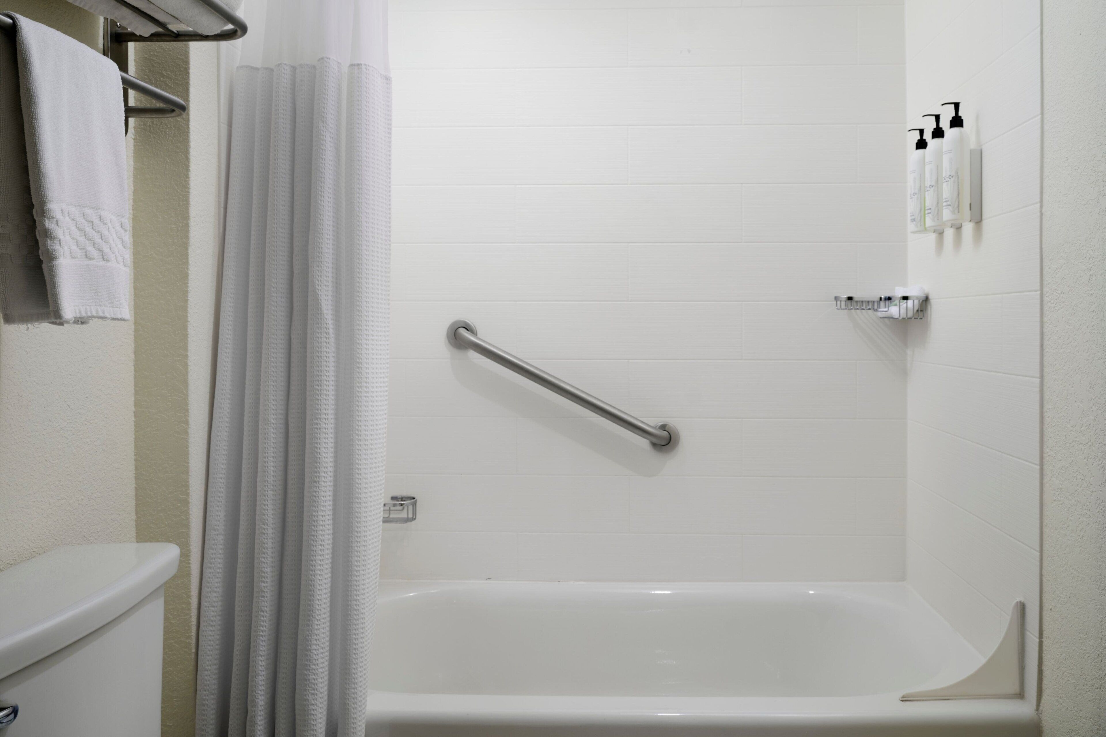 Un baño con una bañera blanca, un pasamanos, un perchero para toallas y artículos de aseo en la pared.