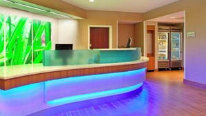 A reception area with a curved counter, a green decorative panel, and a refrigerator stocked with beverages.