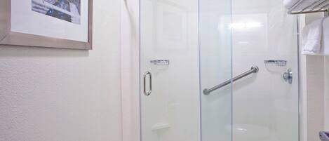 Una ducha con cerramiento de vidrio, un pasamanos, un perchero y un cuadro enmarcado en la pared.