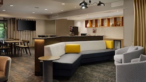 A modern hotel lobby with a seating area, a bar, and a television screen.