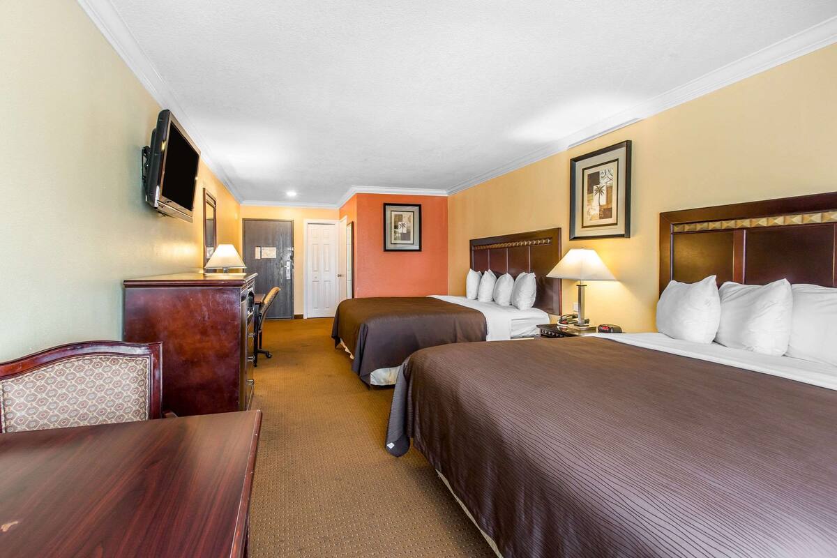 A hotel room with two beds, a desk, a chair, a TV, and a door leading to another room.