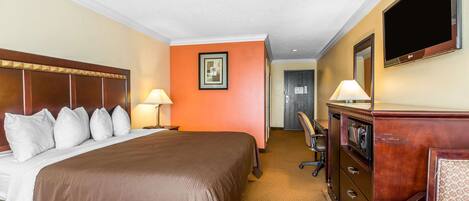 A hotel room with a large bed, a desk, a dresser, a TV, and a framed picture on the wall.