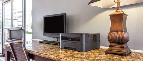A workspace with a desktop computer, a monitor, a printer, and a lamp on a granite countertop.