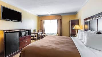 Habitación de hotel con cama, escritorio, televisión de pantalla plana, minibar y ventana con cortinas.