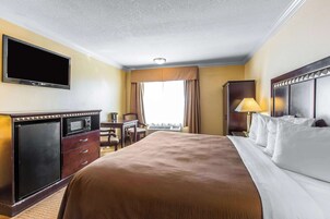 Habitación de hotel con cama, escritorio, televisión de pantalla plana, minibar y ventana con cortinas.