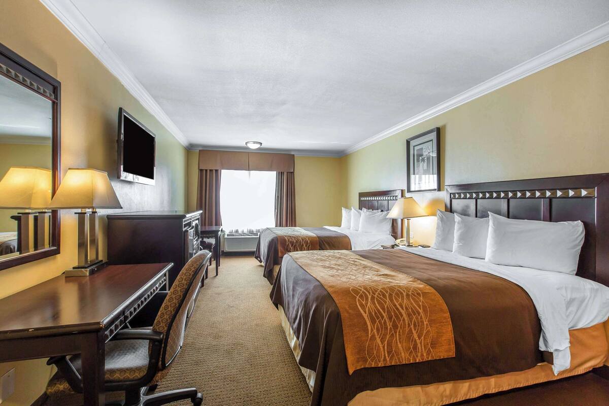 A hotel room with two beds, a desk, a chair, a TV, and a large window.