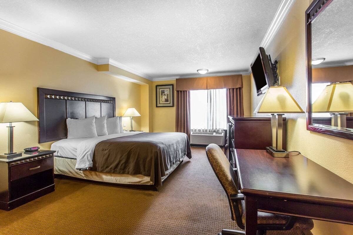 A hotel room with a bed, bedside tables, a desk, a chair, a television, and a large mirror.
