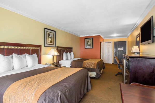 A hotel room with two beds, a desk, a chair, a TV, and a door.