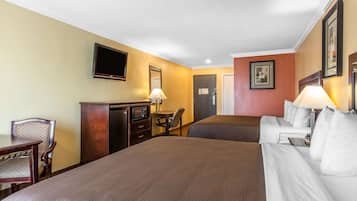 Habitación de hotel con dos camas, un escritorio, una silla, un televisor y una lámpara.