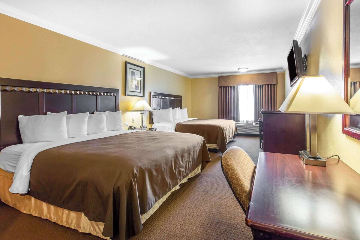 A hotel room with a large bed, a smaller bed, a desk, and a TV.