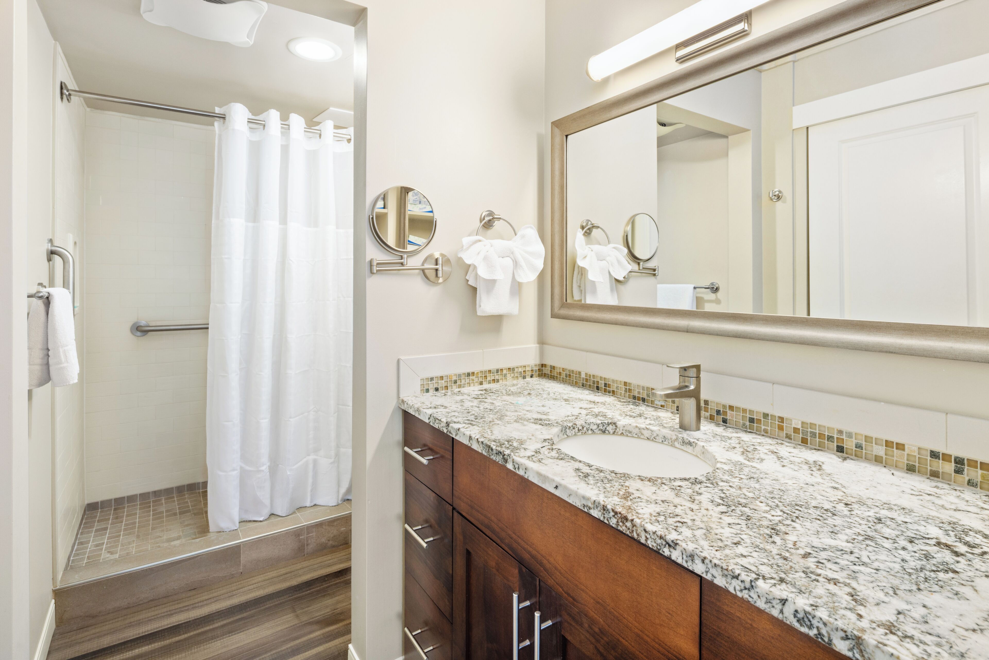 A bathroom with a shower, a sink, a mirror, and a towel rack.