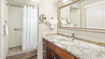 A bathroom with a shower, a sink, a mirror, and a towel rack.