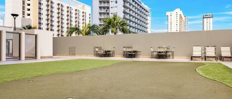 A courtyard with artificial grass, outdoor seating, and a view of high-rise buildings.