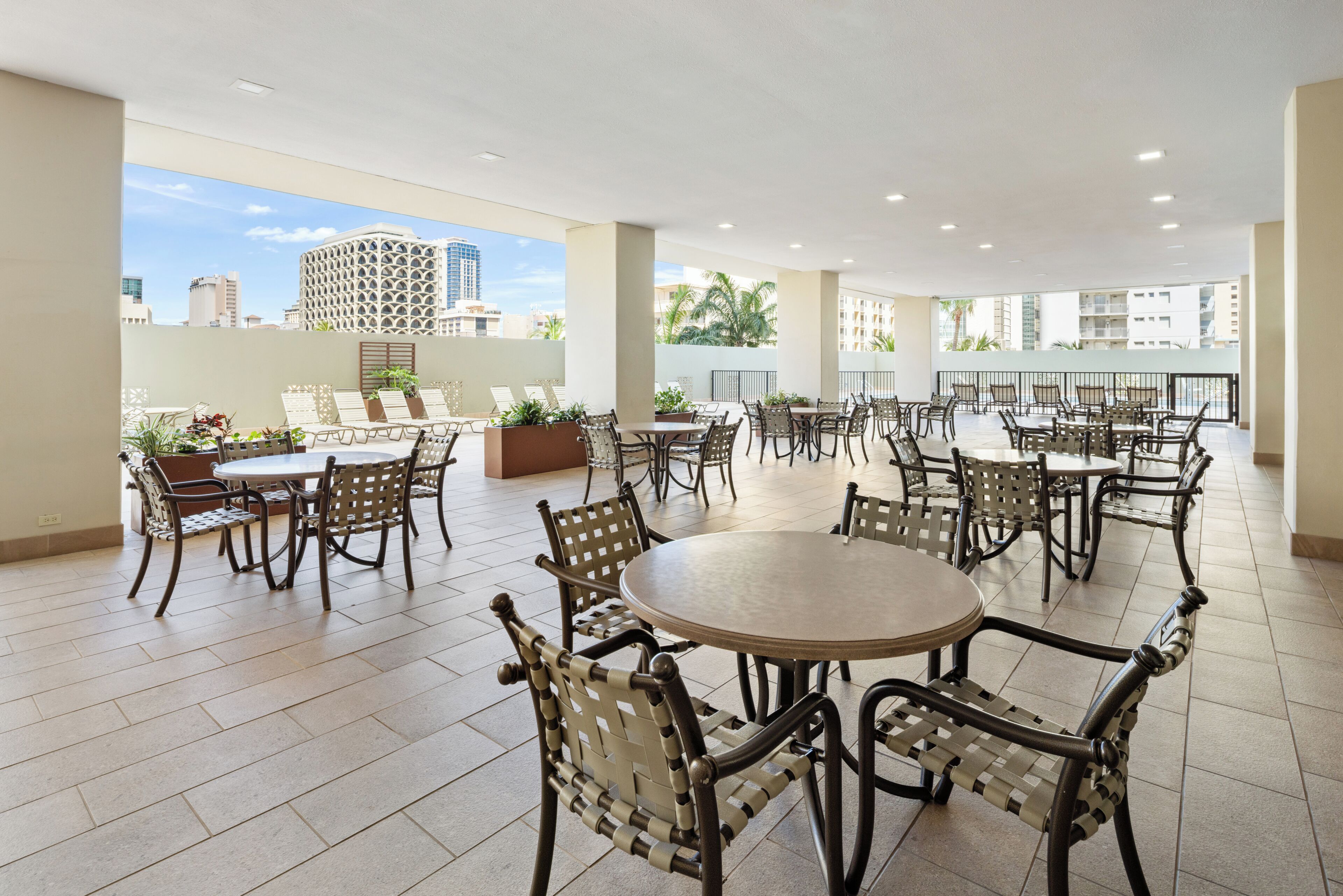 A spacious outdoor patio area with multiple tables and chairs, surrounded by a low wall with potted plants.