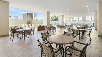 A spacious outdoor patio area with multiple tables and chairs, surrounded by a low wall with potted plants.