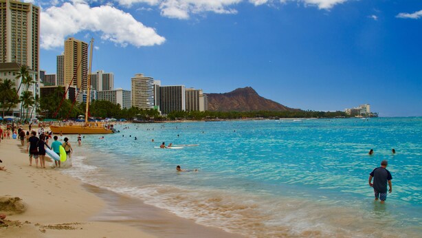 A beach with clear blue water, a city skyline, and a mountain in the background.
