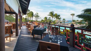 Terraza de restaurante con mesas preparadas para comer, con vista a una piscina y palmeras.