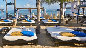 Un resort frente a la playa con numerosas tumbonas dispuestas bajo toldos, cada una con colchón, almohadas y toallas.