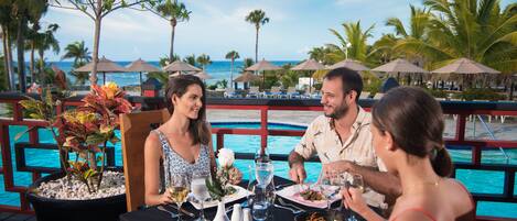 A dining table with a view of the ocean, surrounded by palm trees and umbrellas.