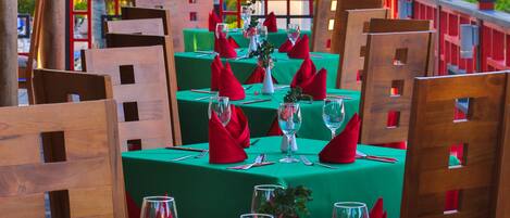 Un restaurante con mesas verdes y servilletas rojas, con palmeras y una barandilla roja de fondo.
