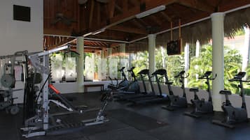 A gym with various exercise equipment, including treadmills and weight machines, under a wooden ceiling with a thatched roof.