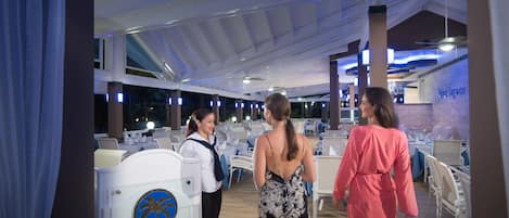 Un amplio comedor interior con mesas y sillas blancas, un techo alto con vigas a la vista, y un letrero que indica el nombre del establecimiento.