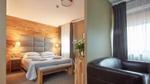 A modern bedroom with a wooden headboard, a bed with white bedding, a bedside table with a lamp, and a window with sheer curtains.
