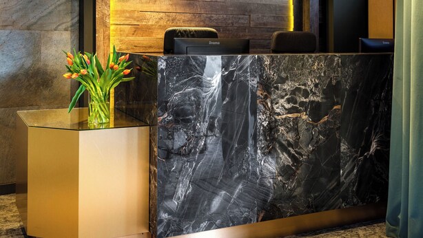 A reception desk with a marble top, a wooden wall with a reception sign, and pendant lighting.