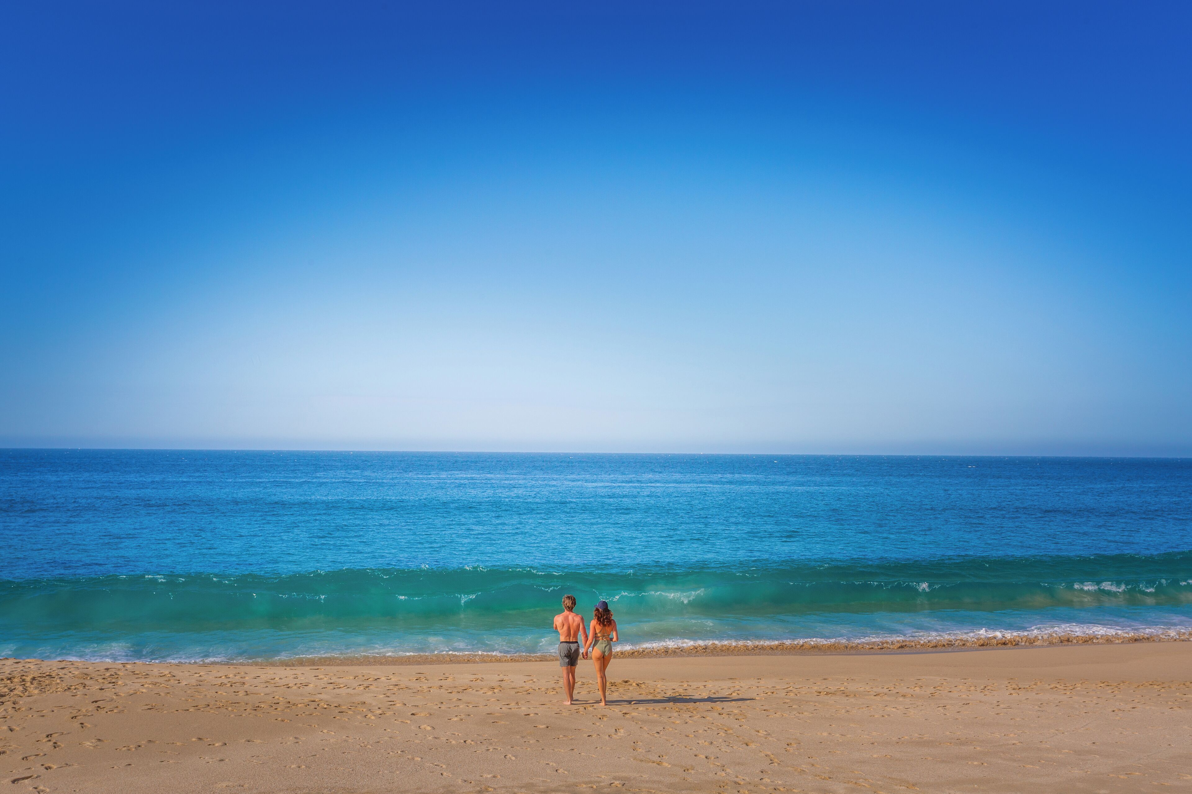 A beach with two people walking towards the ocean.