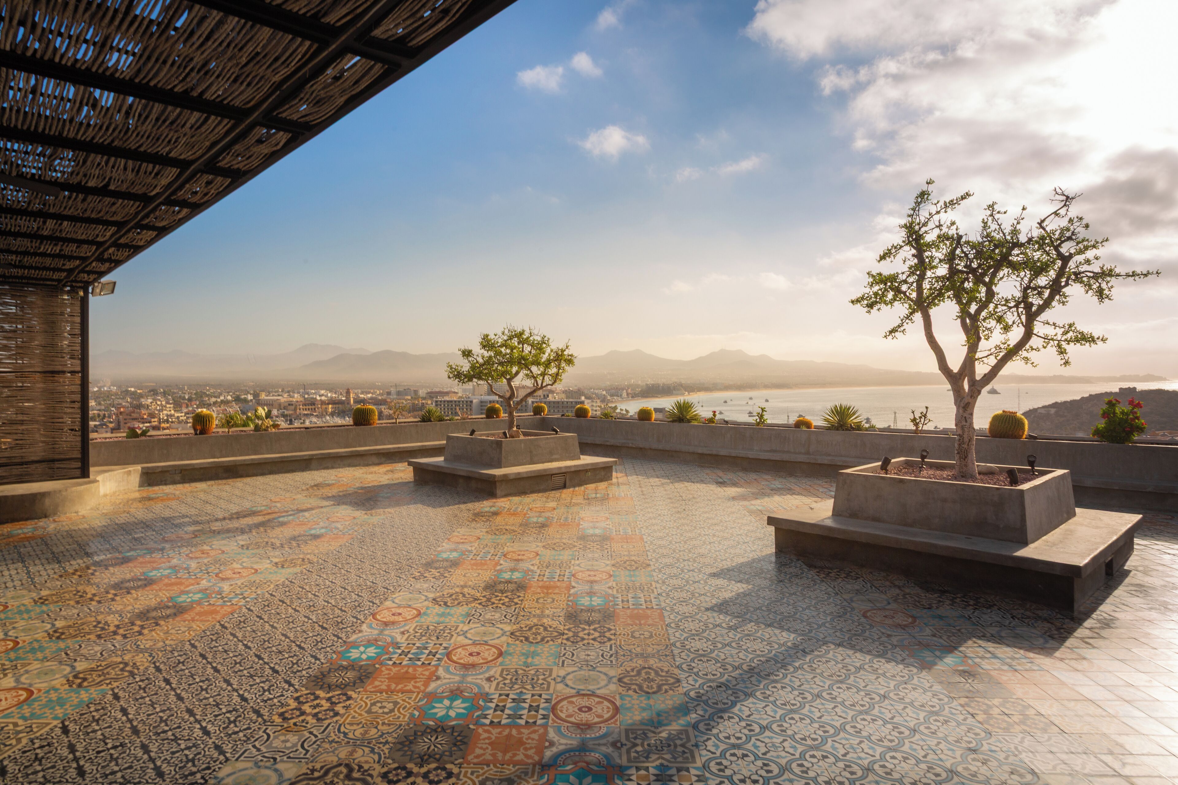 A rooftop terrace with patterned tiles, potted plants, and a view of the city and mountains.