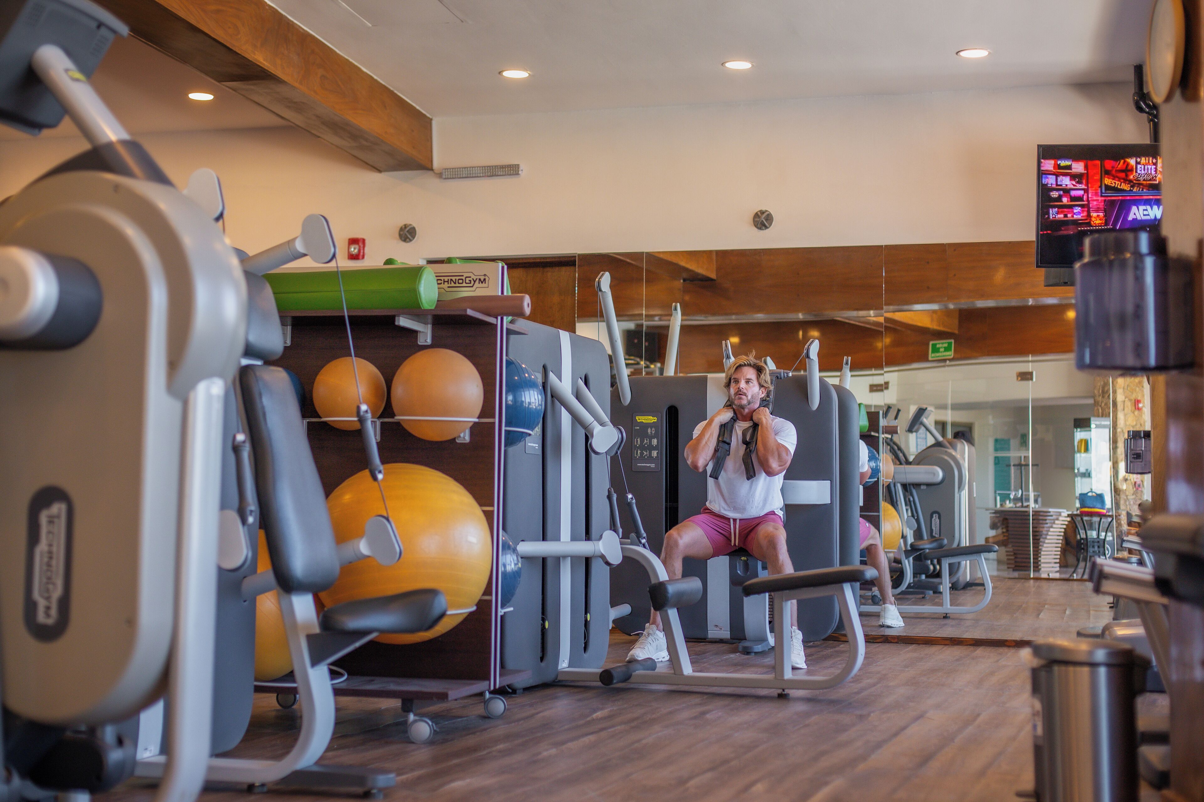 A gym with exercise equipment, a television, and wooden flooring.
