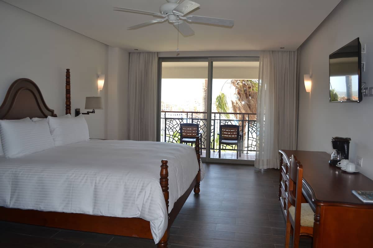 A hotel room with a large bed, a desk, a ceiling fan, and a balcony with chairs.