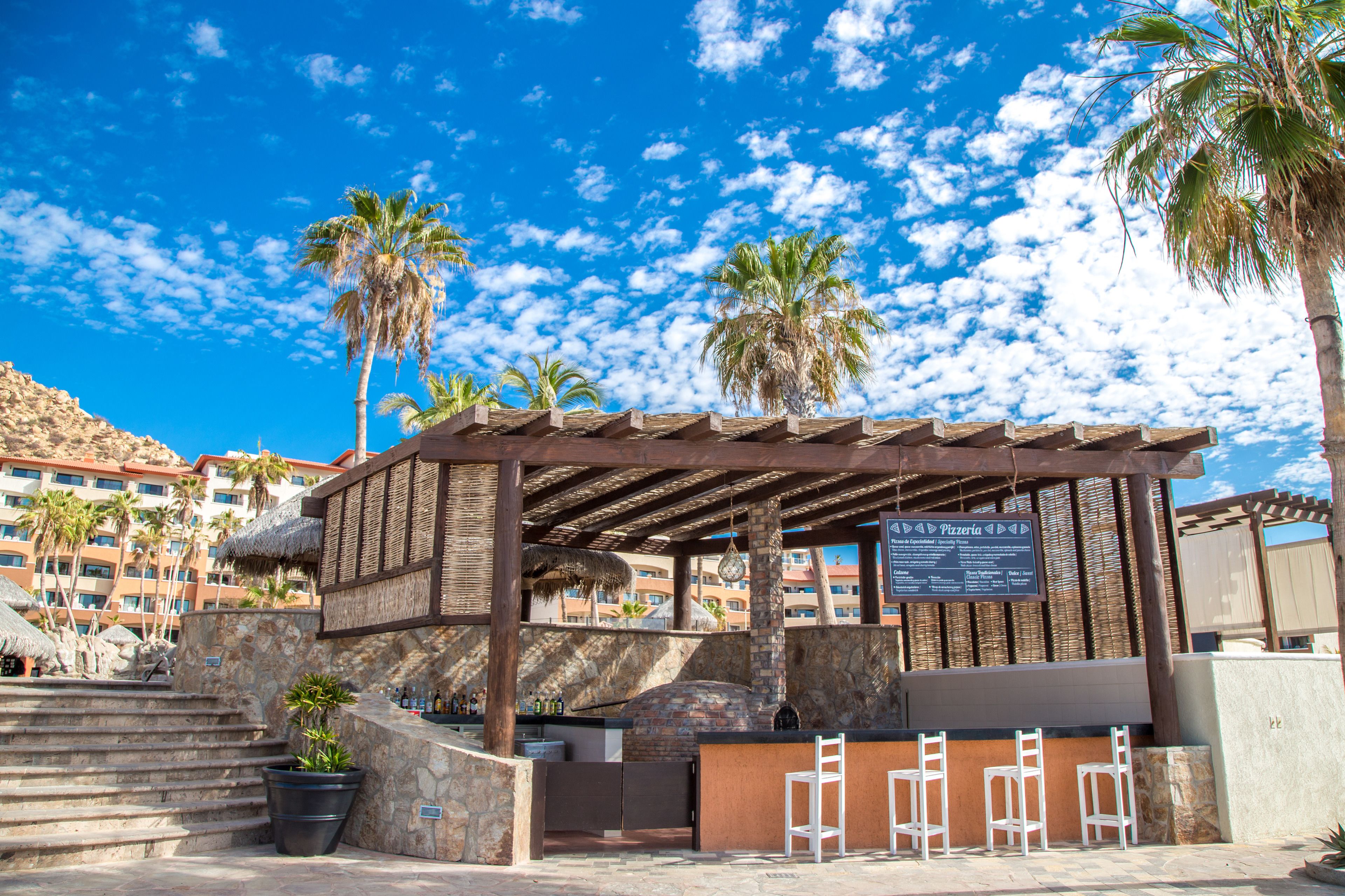 Un espace extérieur aménagé avec une pergola, un panneau indiquant un restaurant et des palmiers.