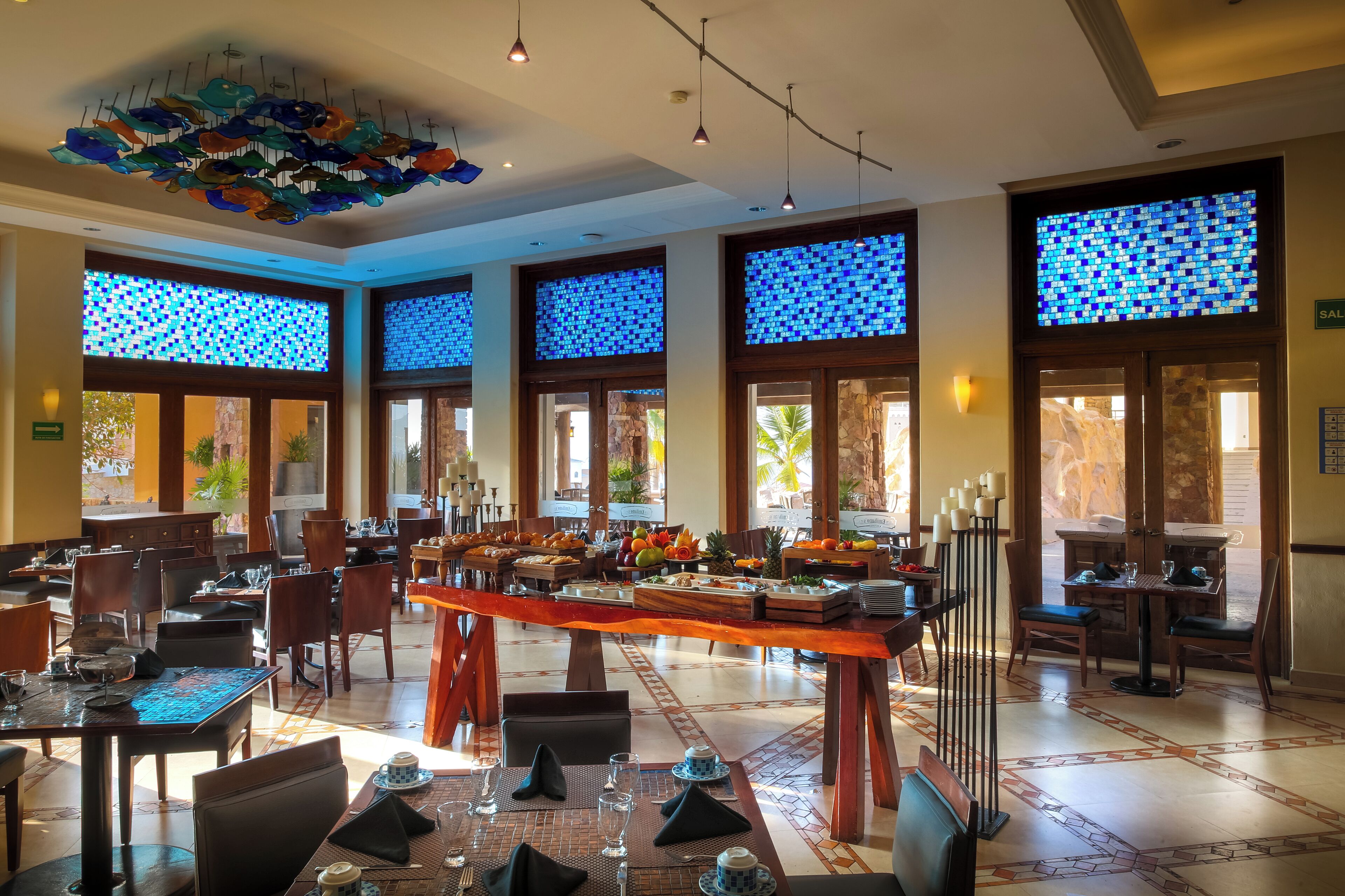 A hotel dining area with a buffet, large windows with blue-tinted glass, and a decorative ceiling.