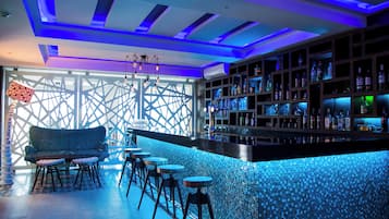 A bar area with a blue-tiled bar counter, a seating area with a sofa and stools, and a patterned wall.