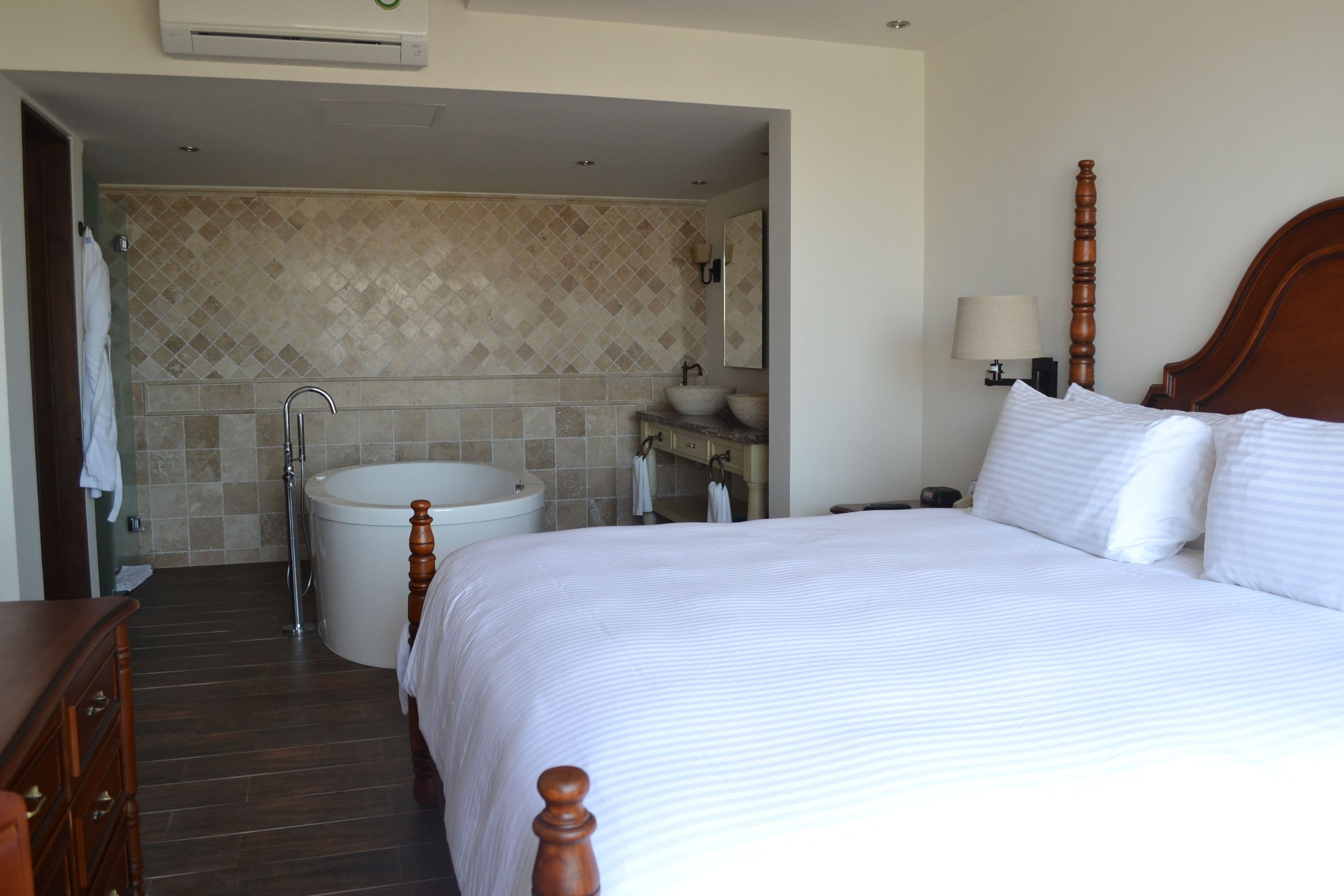 Una habitación de hotel con una cama grande, un baño con lavabo e inodoro, y un aparador de madera.