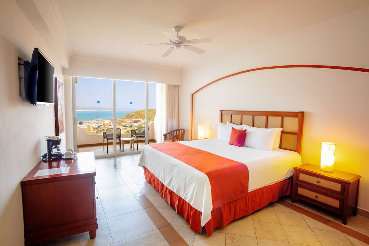 Ein Hotelzimmer mit Bett, Schreibtisch, Nachttisch, Fernseher und Meerblick.