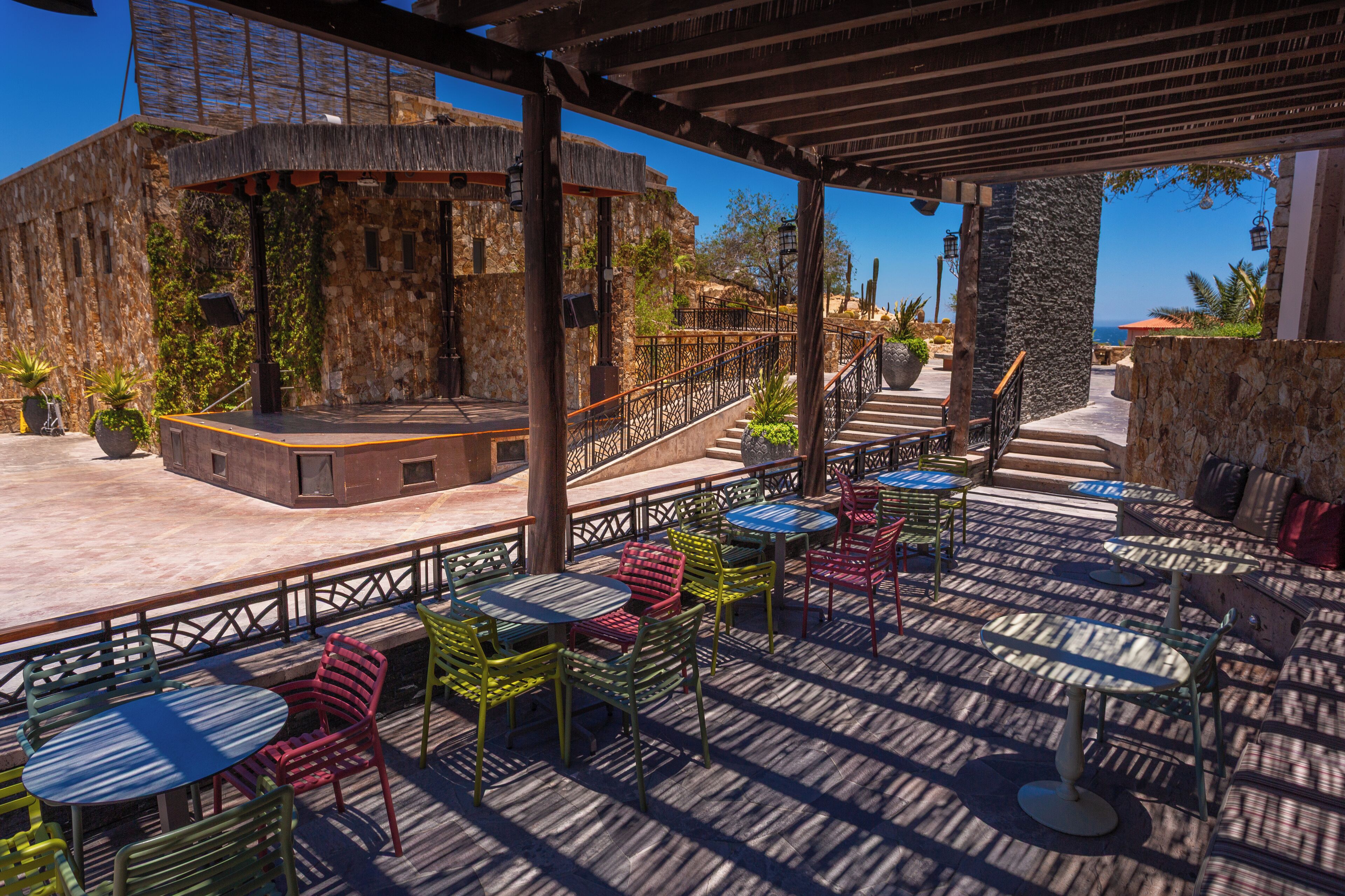 An outdoor patio area with multiple tables and chairs, a stage, and a view of the ocean.