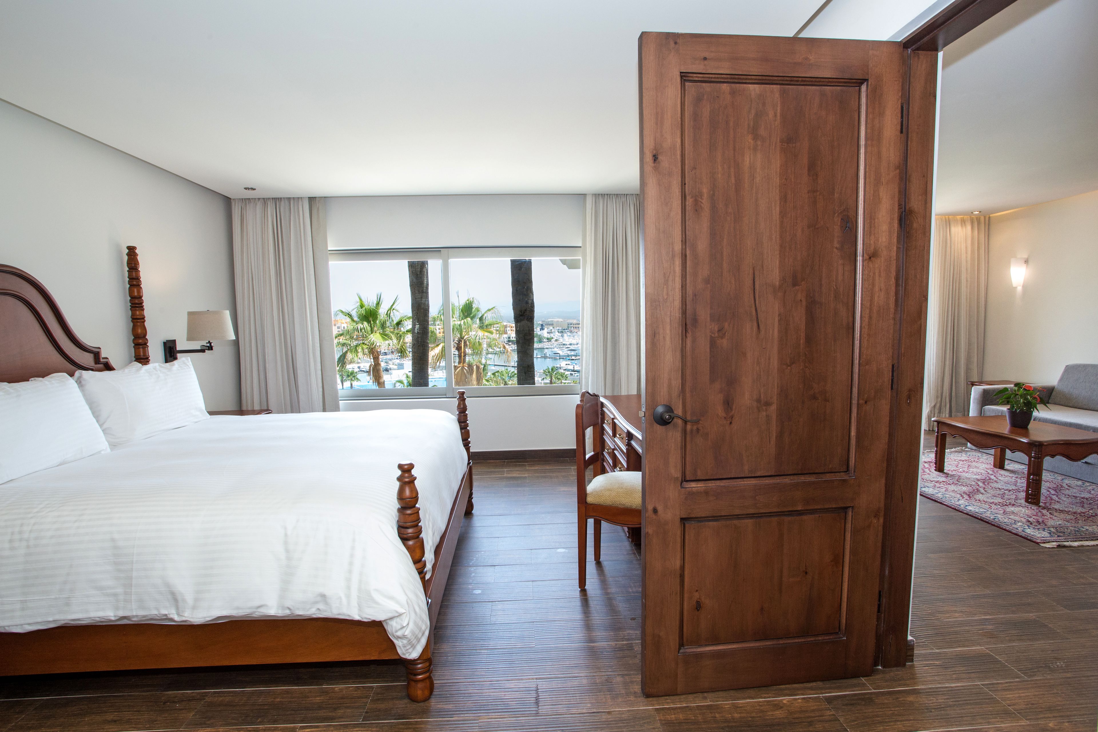 A hotel room with a large bed, a wooden door, a view of the city, and a small seating area.