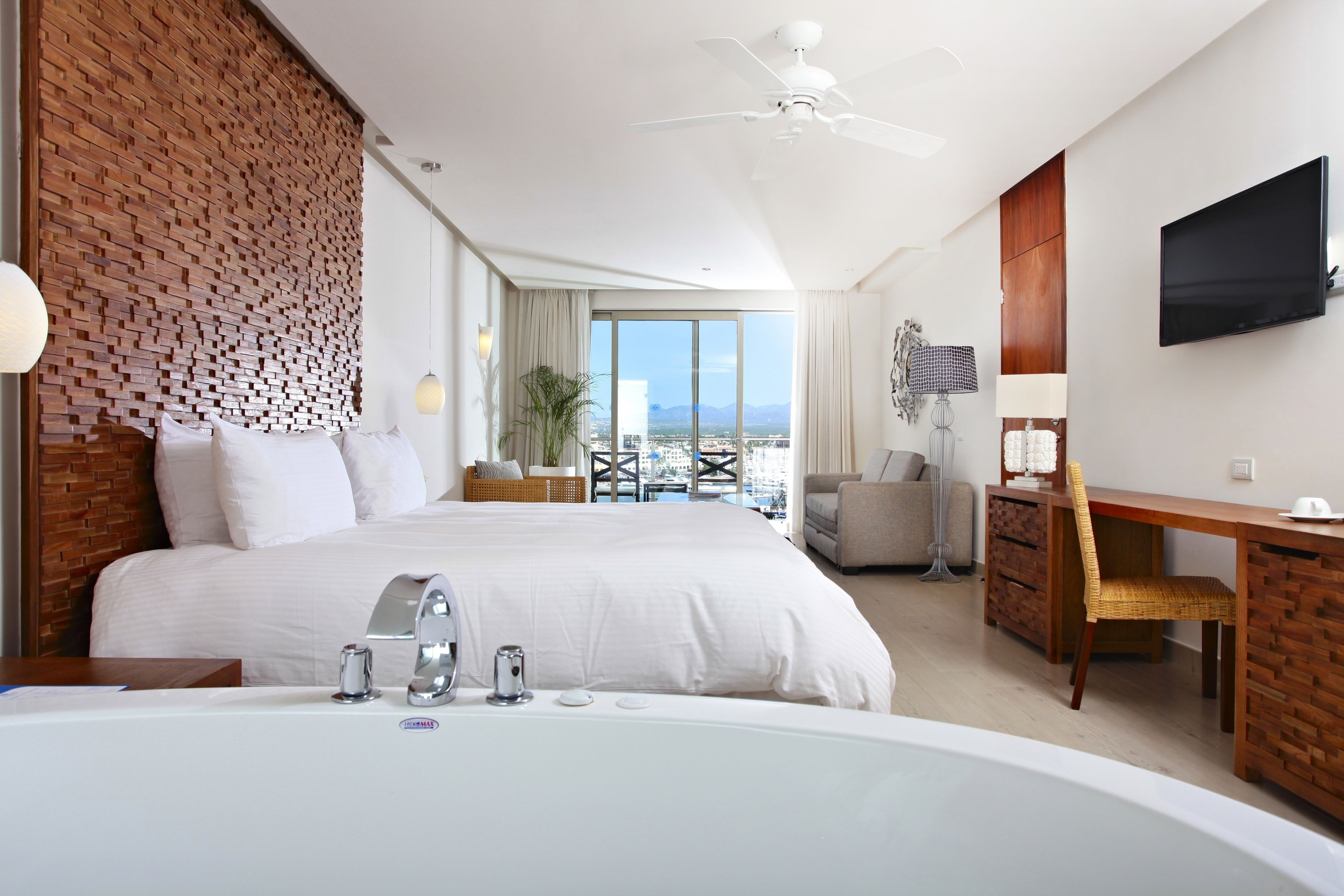 Ein modernes Hotelzimmer mit einem großen Bett, einem Schreibtisch, einem Flachbildfernseher, einem Deckenventilator und Blick auf die Stadt.