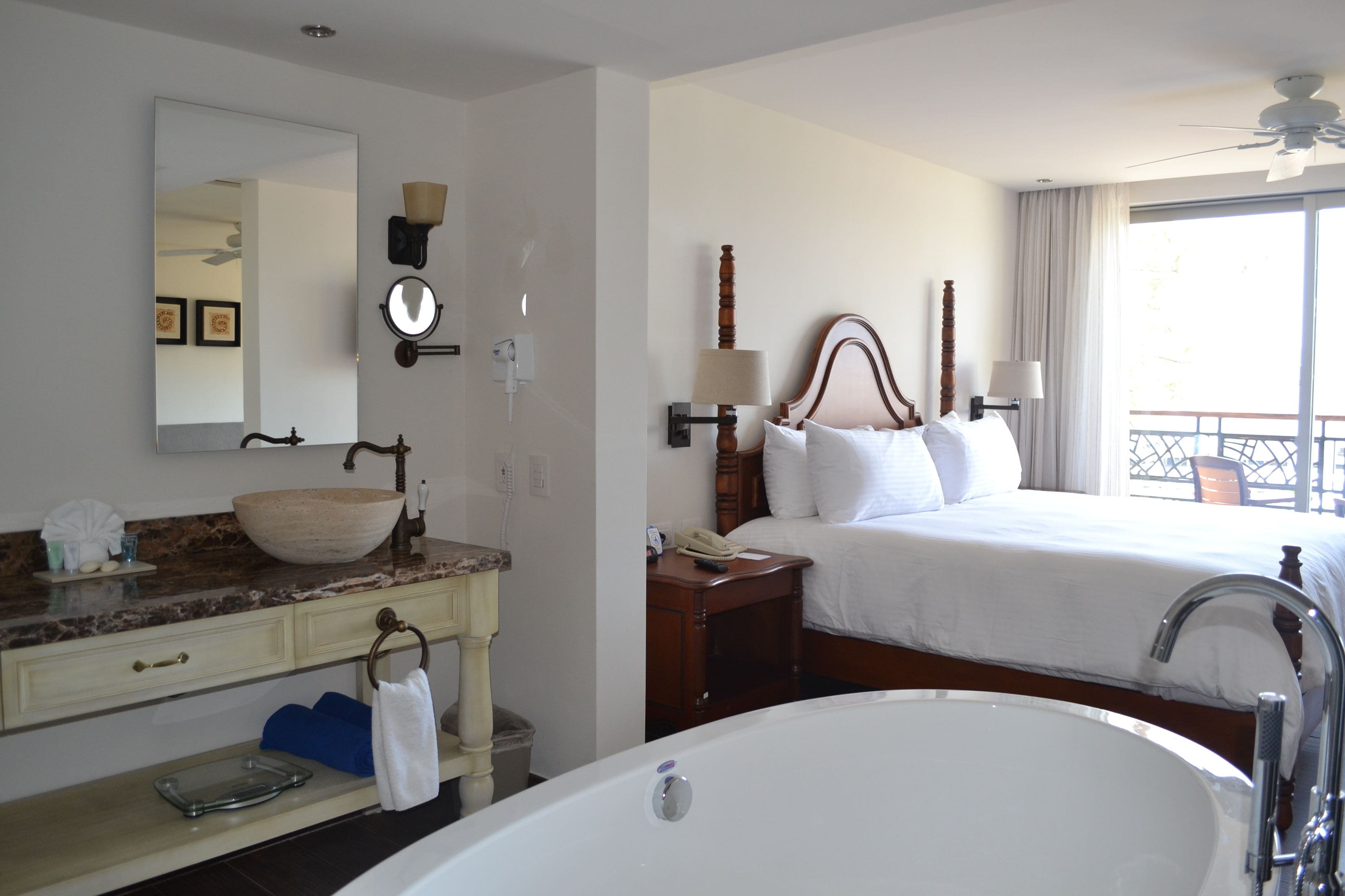 Una habitación de hotel con una cama grande, un baño con bañera, tocador con lavamanos y un espejo grande.