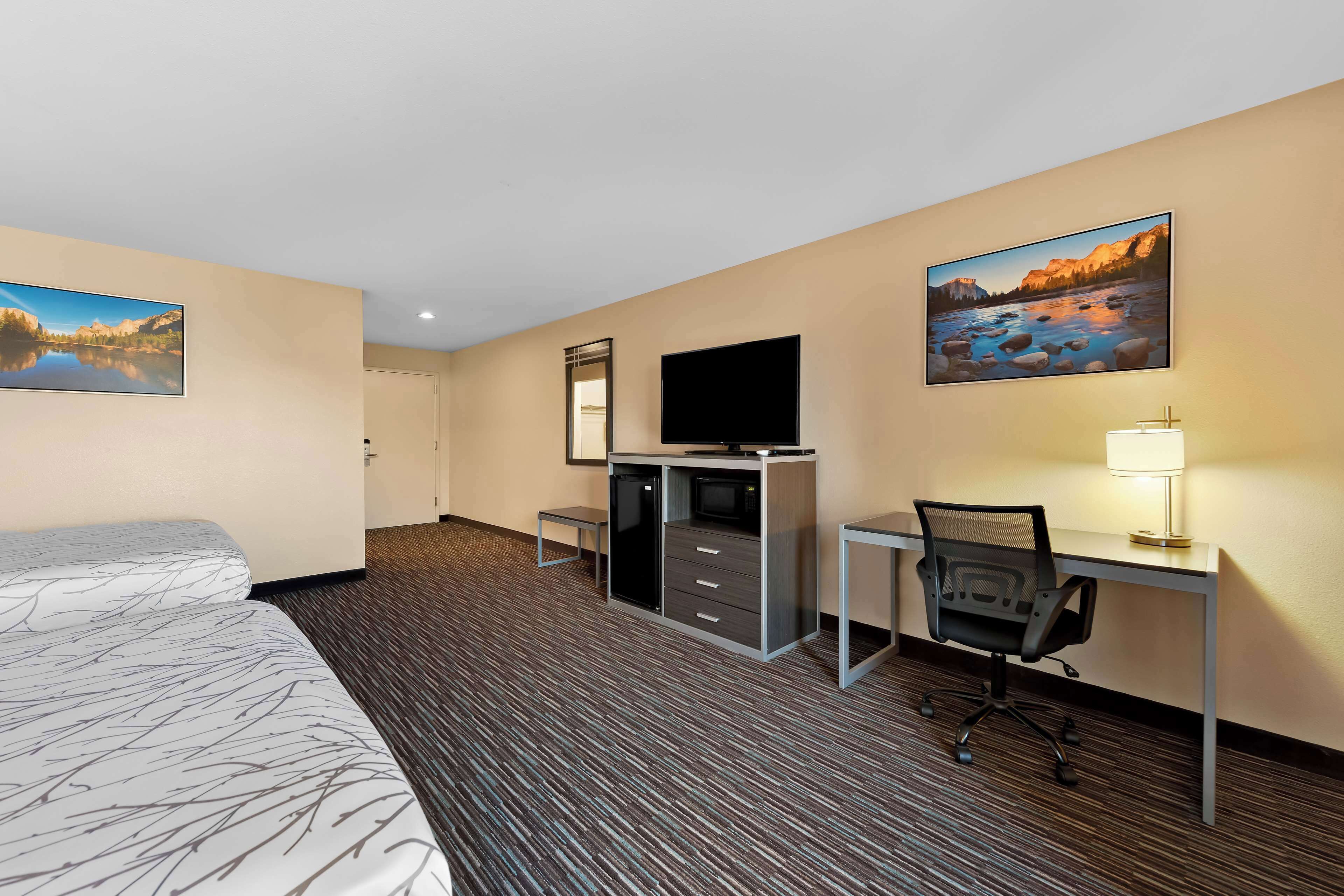 A hotel room with two beds, a desk with a chair, a TV, a desk lamp, and two paintings on the walls.