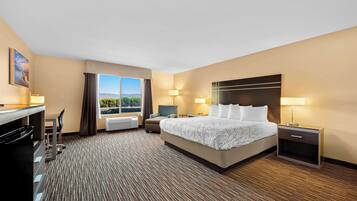 A hotel room with a large bed, a desk, a chair, a nightstand, and a window with a view of the outdoors.
