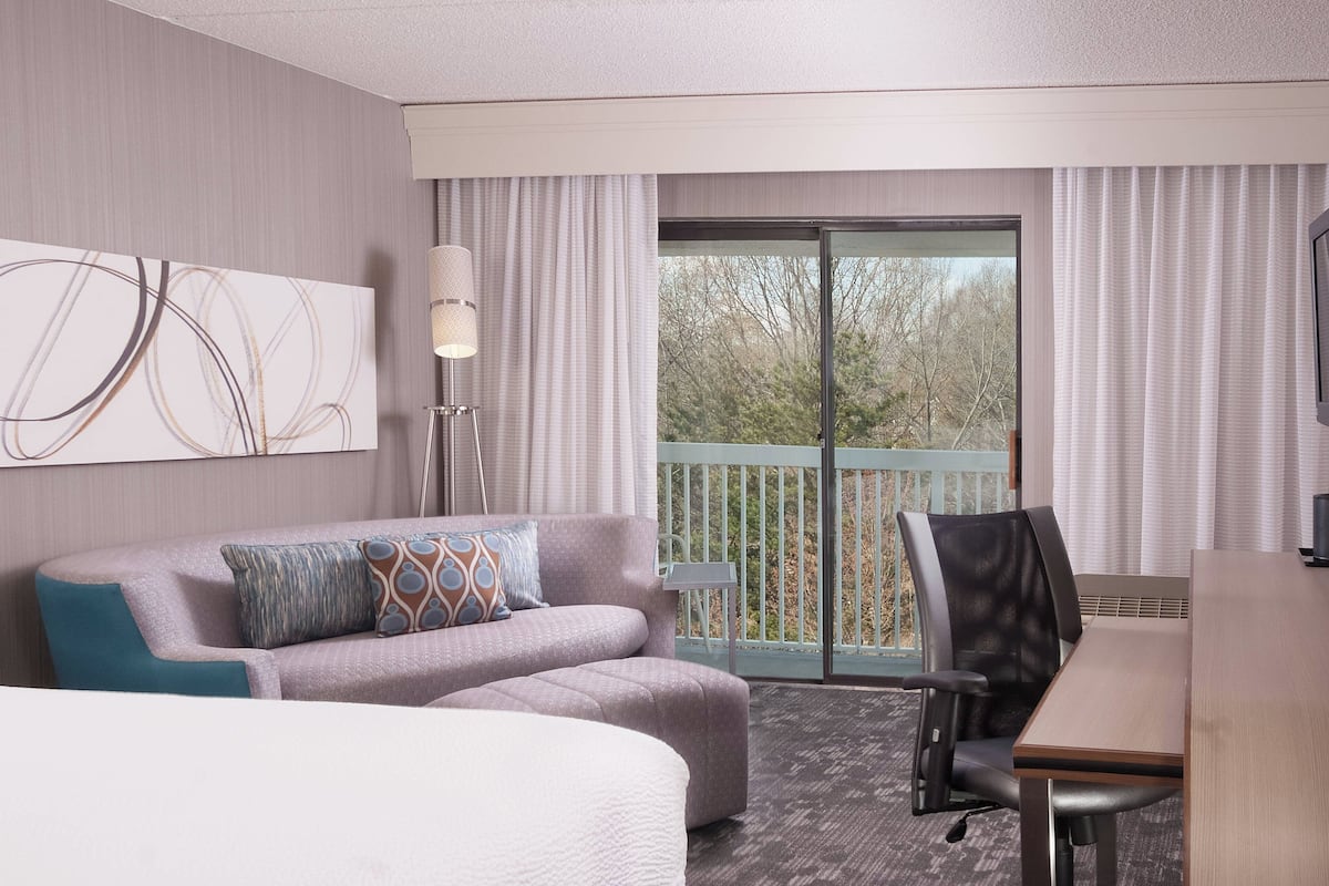 Une chambre d’hôtel comprenant un lit, un canapé, une table à manger et un balcon avec vue sur les arbres.