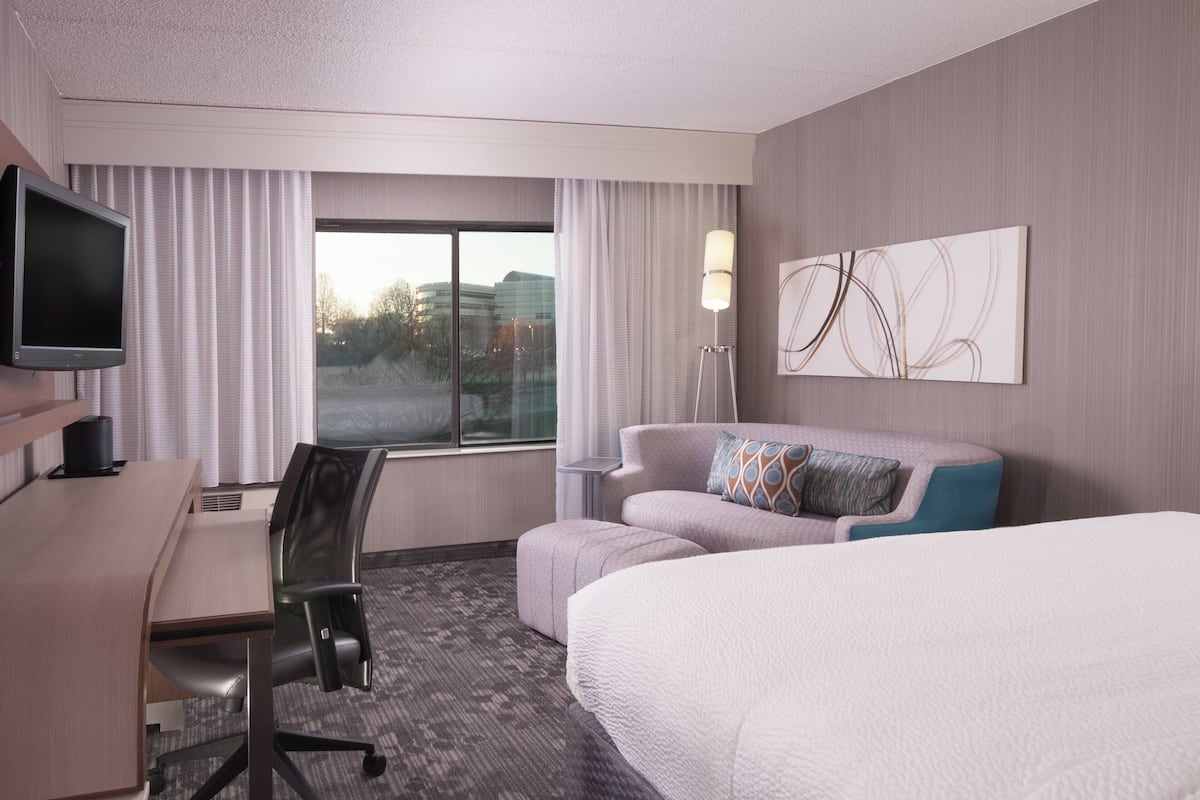 Une chambre d’hôtel comprenant un lit, un bureau avec un ordinateur, une chaise, un canapé, une télévision et une fenêtre avec des rideaux.